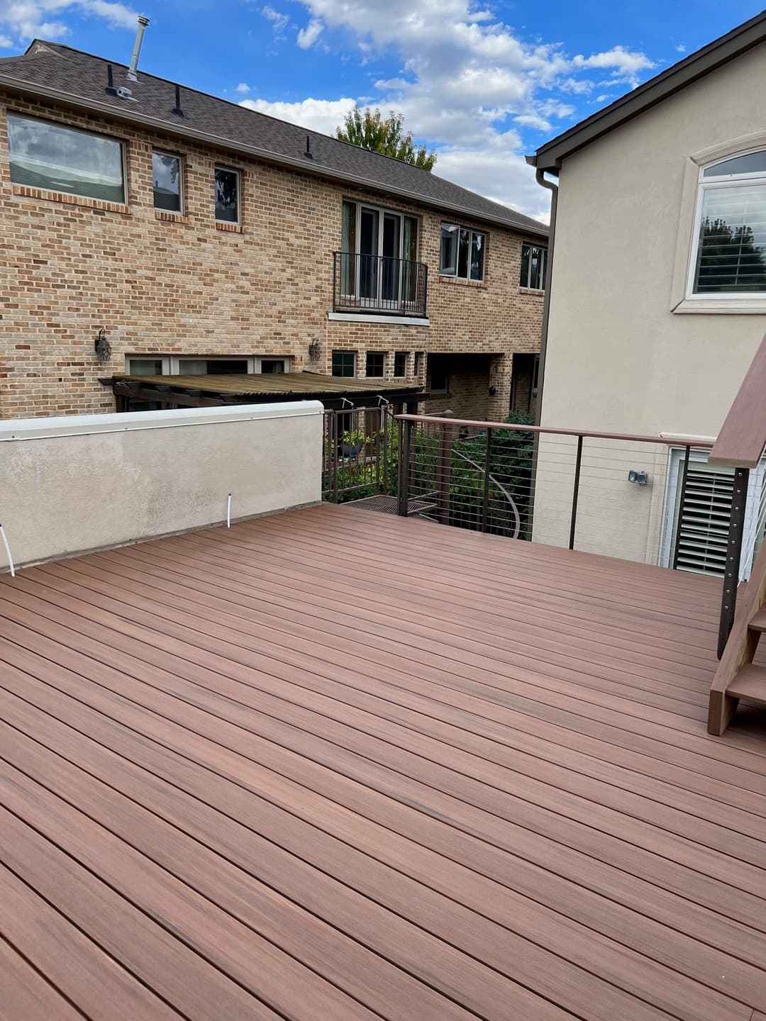 Composite deck with brown boards overlooking a two-story brick house and blue sky.