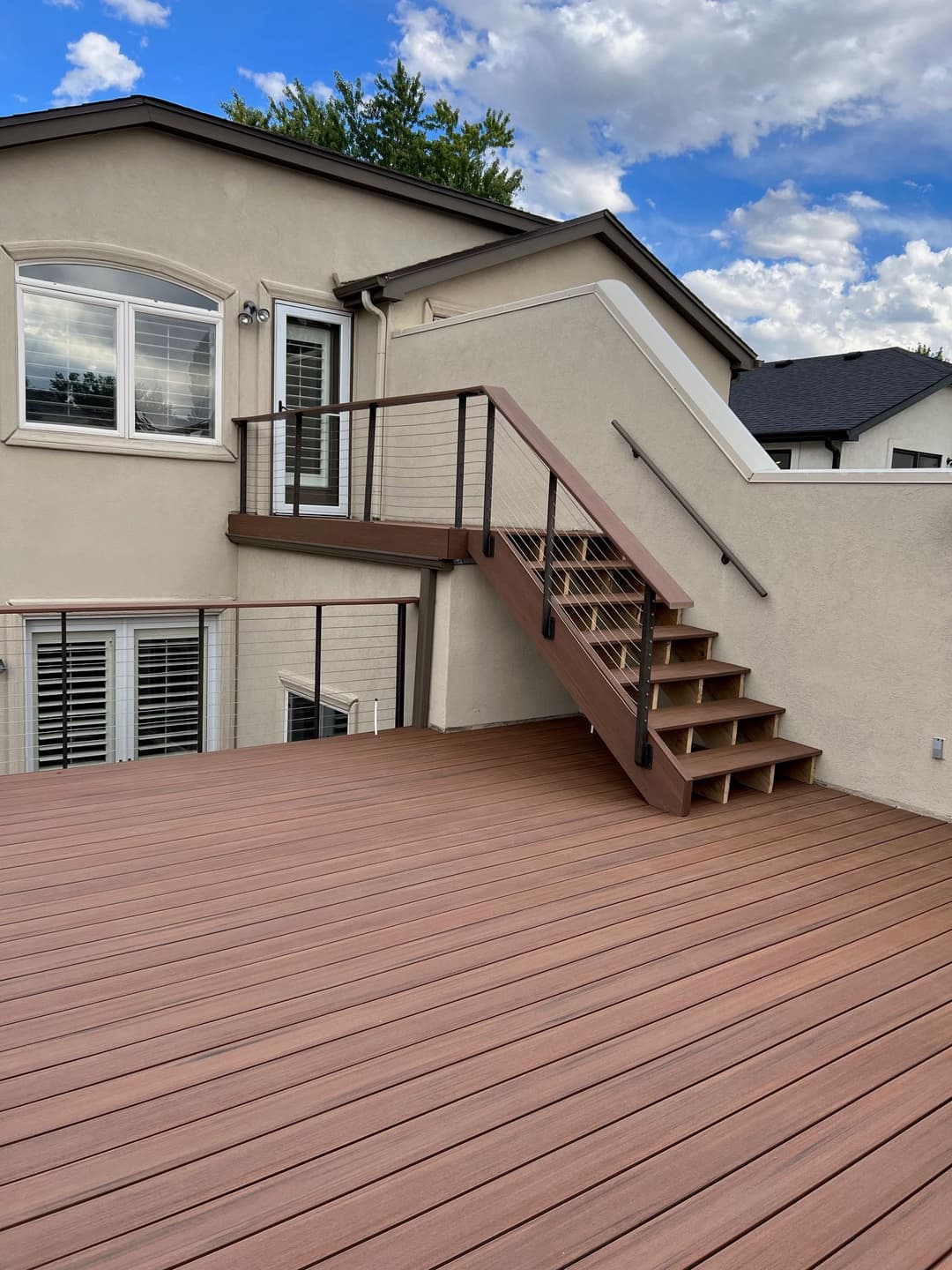 Modern composite deck with brown railing and stairs, surrounded by a residential home.