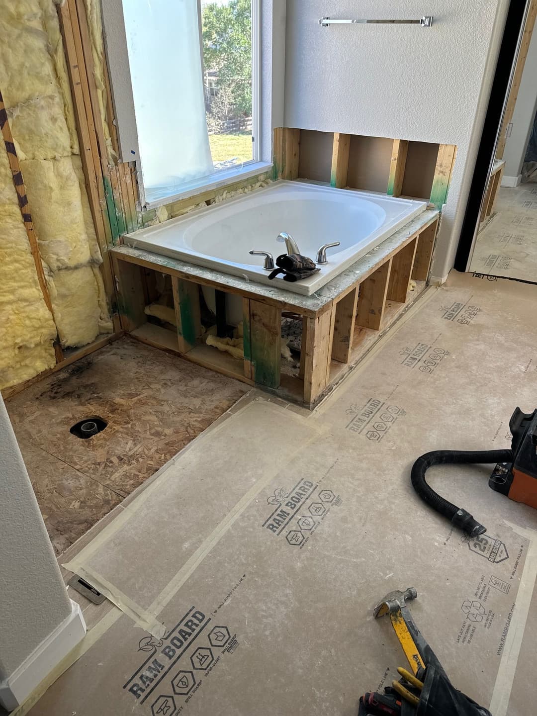 Bathroom renovation featuring a bathtub installation with exposed framing and construction tools.