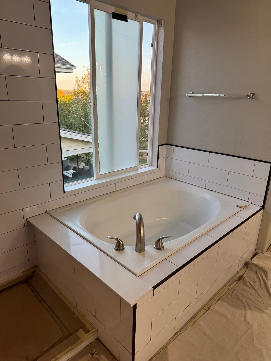 Modern bathroom with a corner soaking tub, large window, and white subway tile.