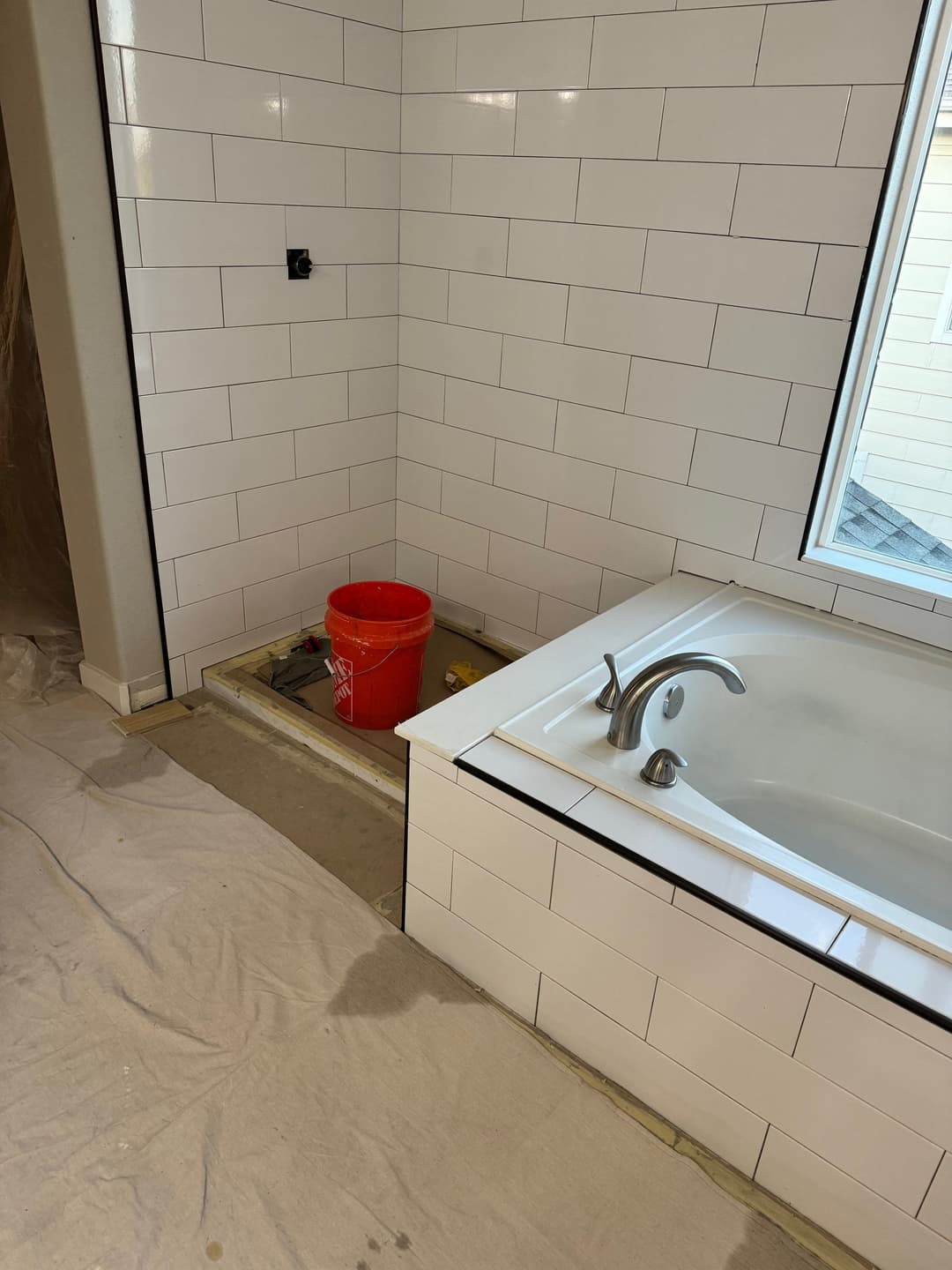 Renovated bathroom featuring a bathtub, tiled walls, and a construction area with a bucket.