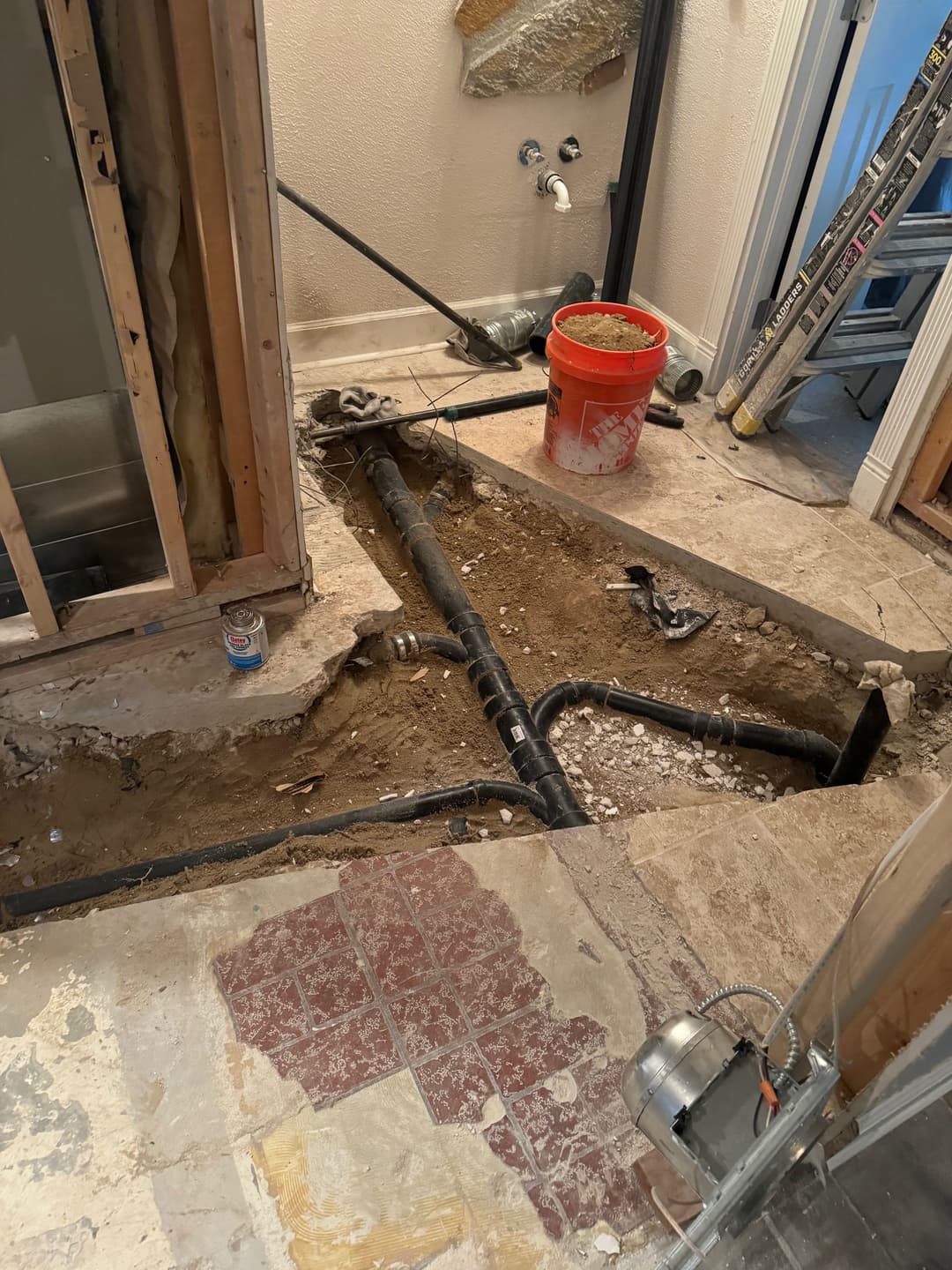 exposed plumbing and renovation site with orange bucket and ladder in unfinished bathroom