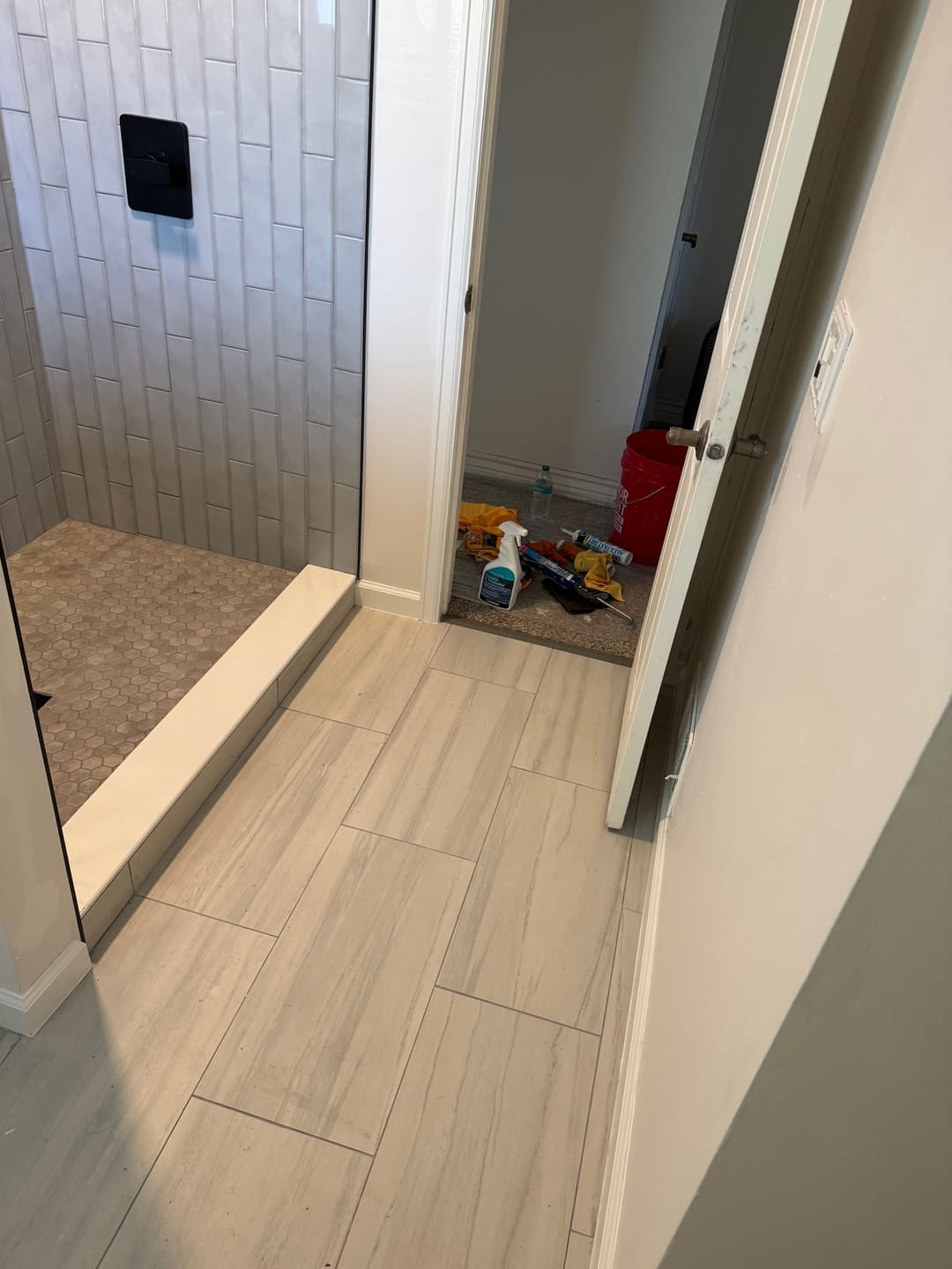 Bathroom interior showing a tiled shower, clean floor, and clutter near the doorway.