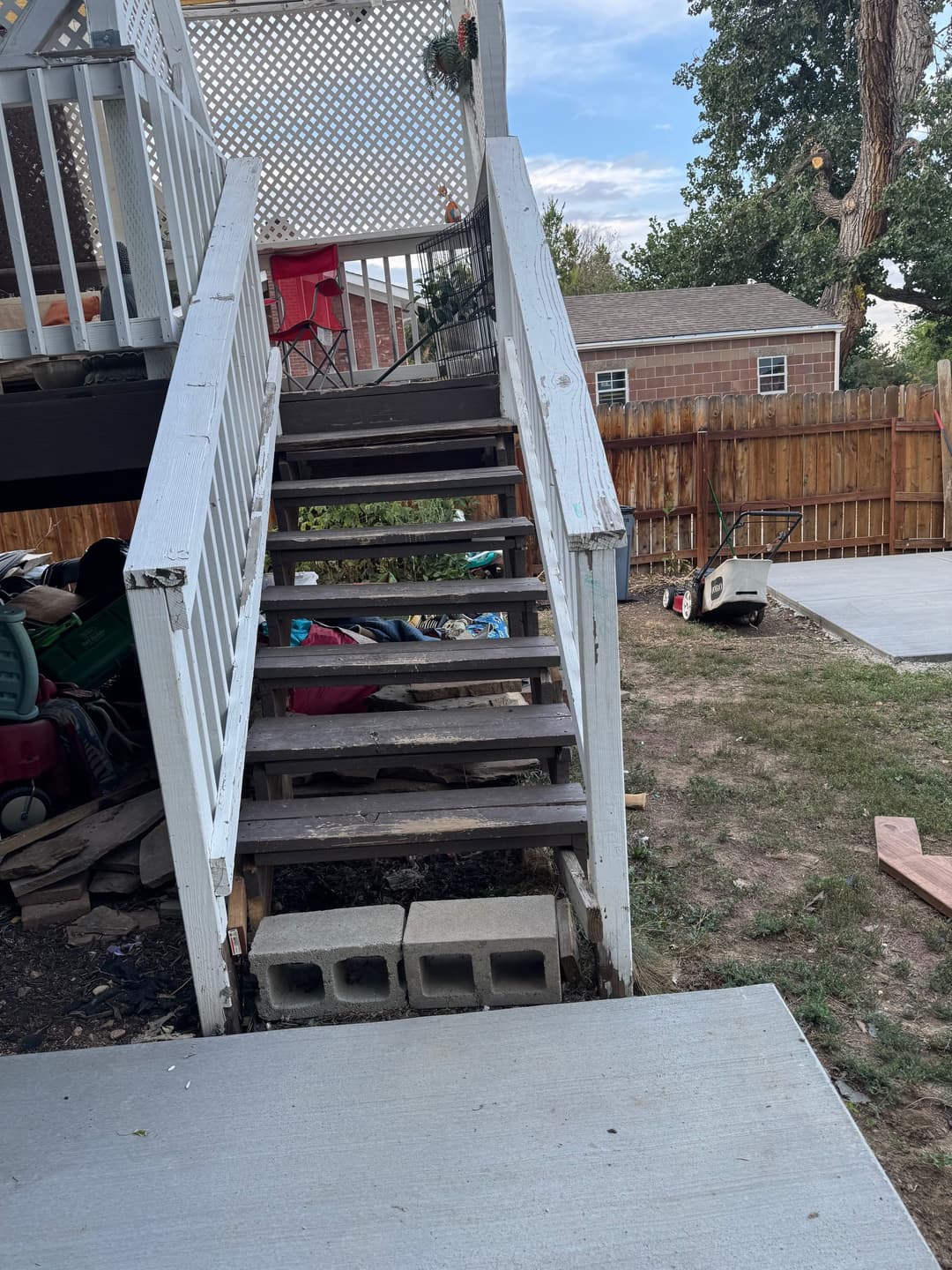 Stairs leading to a deck in a backyard with scattered outdoor furniture and clutter.