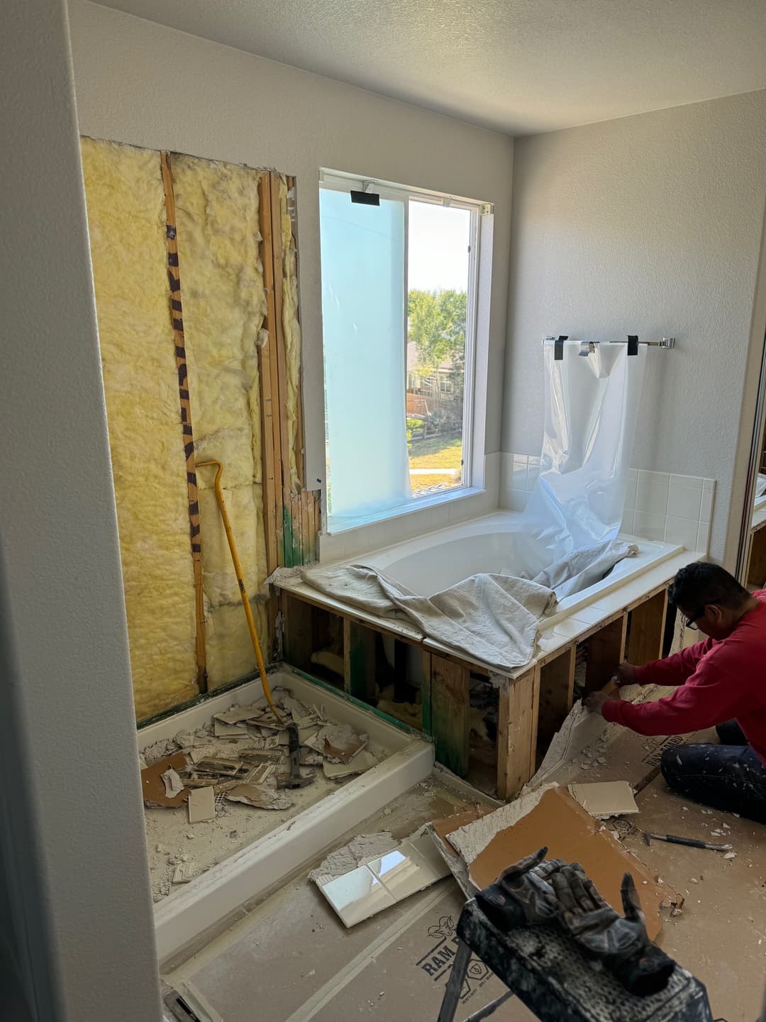 Bathroom renovation in progress with construction debris, exposed walls, and a worker.