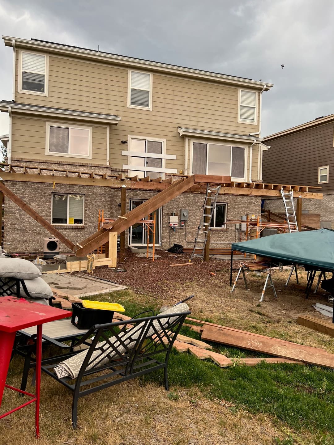 Residential backyard construction with an elevated deck under construction. Tools and materials visible.