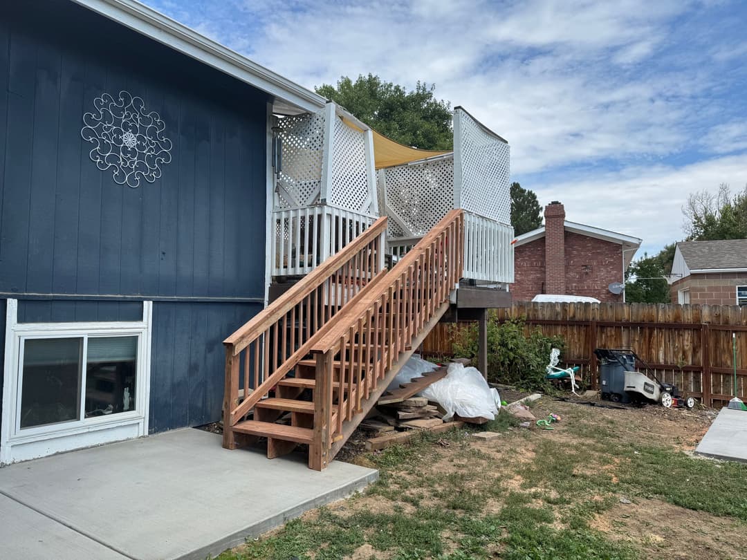 Backyard view of a house with wooden steps leading up to a porch, surrounded by a fence.