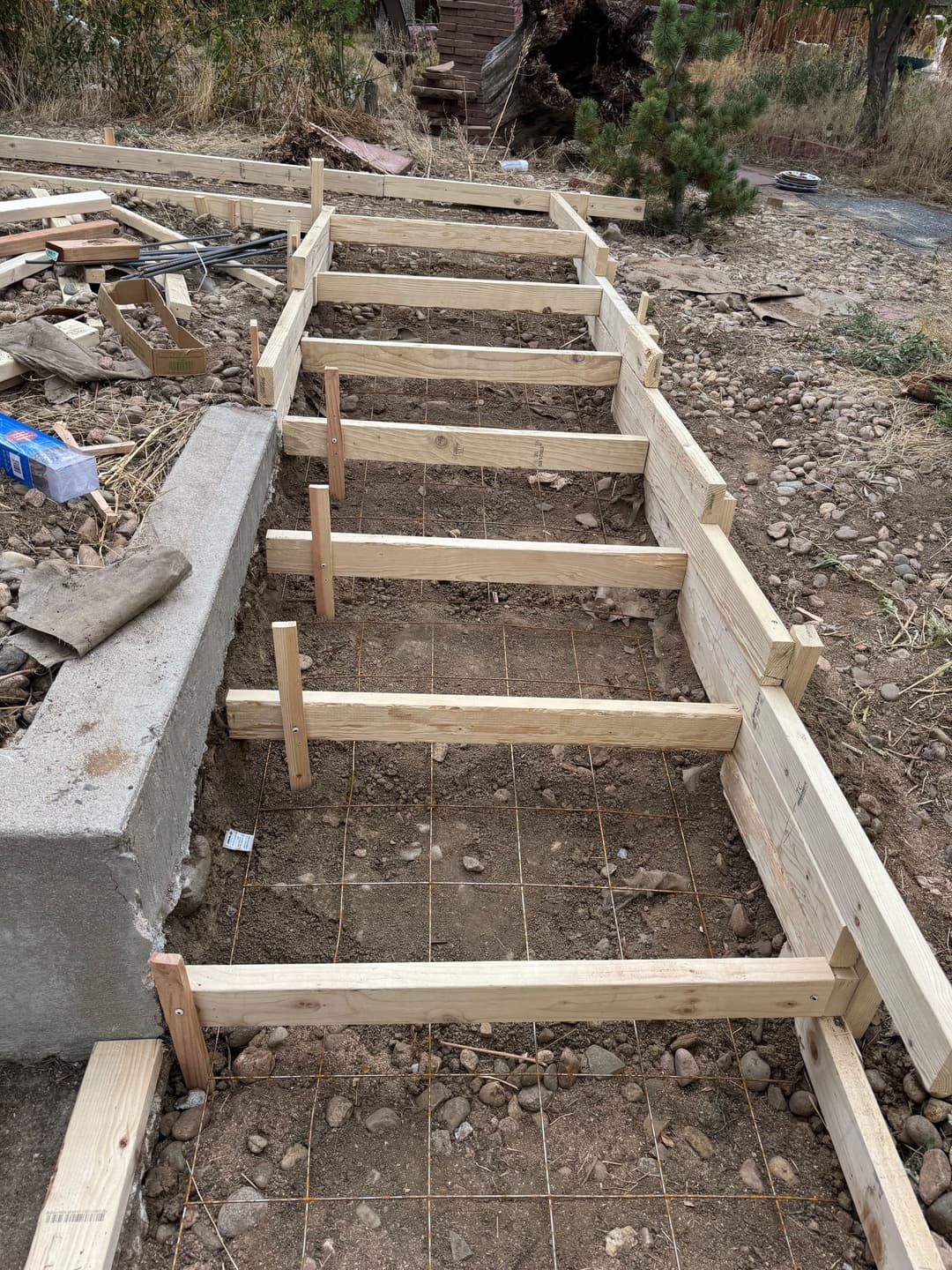 Wooden framing structure for concrete pathway under construction in a landscaped area.