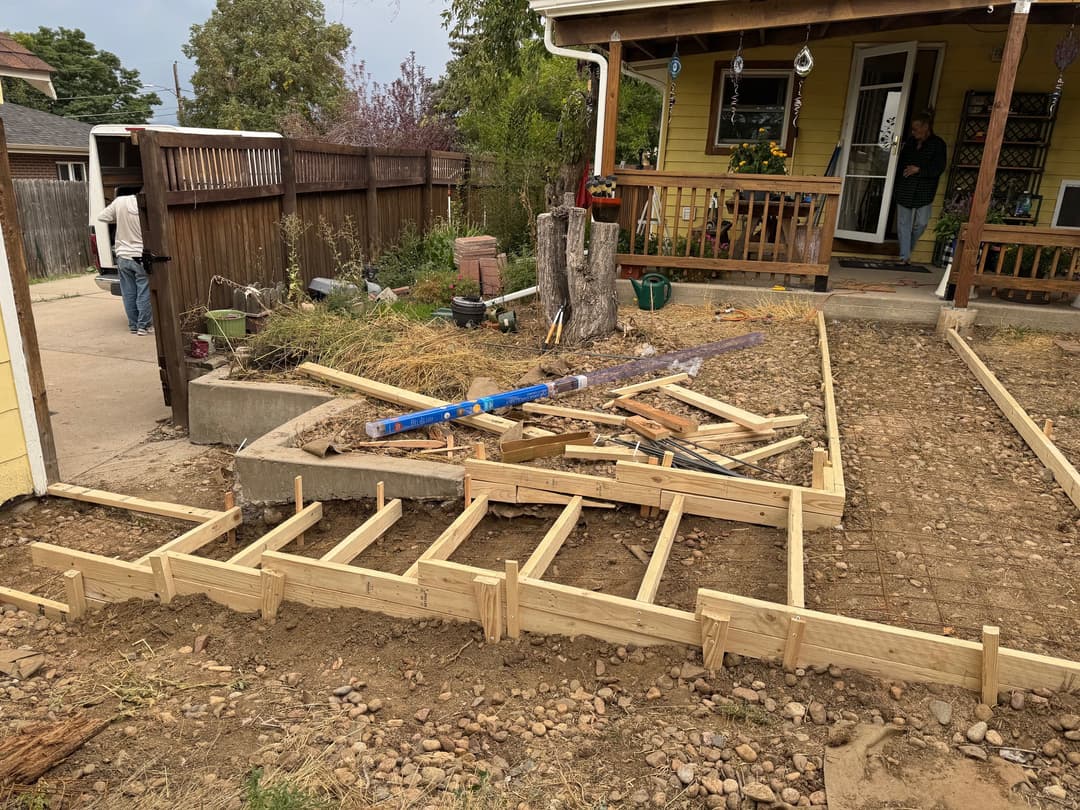 Construction site with wooden framing for a porch, tools, and a house in the background.