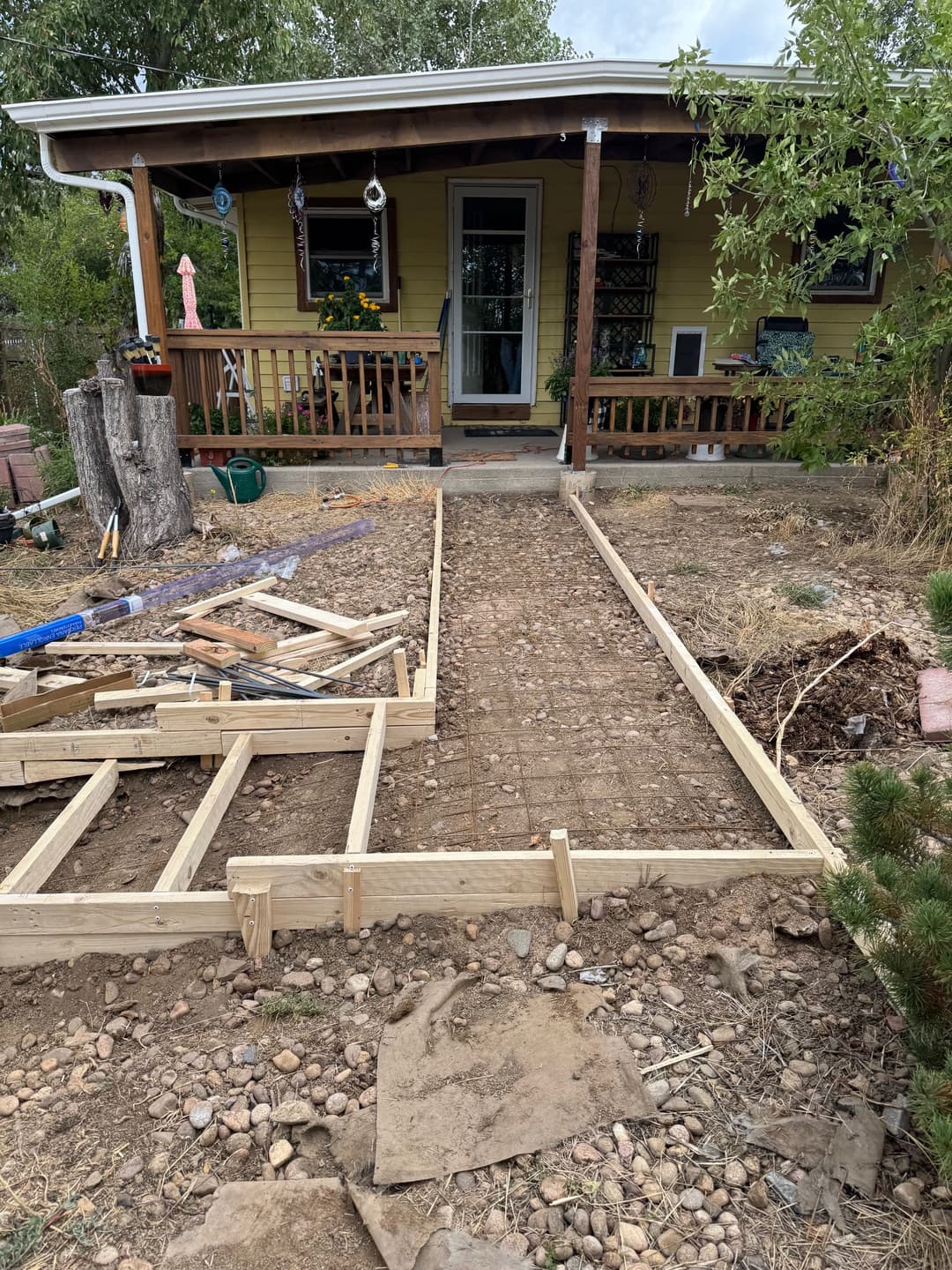 Construction site featuring a newly framed pathway leading to a yellow house with a porch.